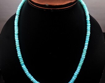 May include: A turquoise beaded necklace displayed on a black mannequin. The necklace is composed of small, round beads, creating a continuous strand. The beads have a consistent color and size, and the necklace is draped in a gentle curve.