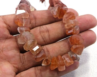 May include: A strand of faceted, translucent, orange-brown gemstone beads. The beads are irregular in shape and have a slightly cloudy appearance.