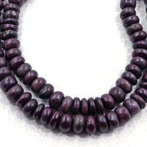 May include: A strand of dark purple gemstone beads. The beads are round and have a slightly irregular shape. The beads are strung on a clear thread.