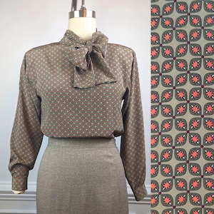 May include: A green and brown patterned blouse with a large bow tie. The blouse has long sleeves and a high neck. The pattern is a repeating geometric design with red accents.