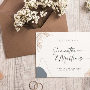 Peut inclure: Une carte blanche avec des formes abstraites brunes et bleues et des illustrations florales dor&eacute;es. Le texte sur la carte indique "Save the Date" suivi de "Samantha & Martinus" et "6 PM in the evening, Lyon, France 1299".