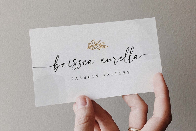 Peut inclure: Une carte de visite blanche avec le texte "baissca aurella FASHION GALLERY" en &eacute;criture cursive noire. Un motif de feuille d'or se trouve au-dessus du texte.