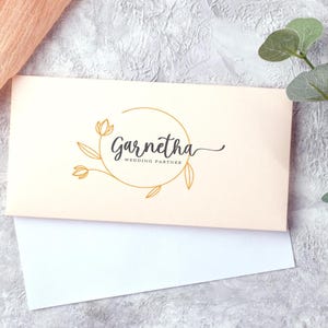 May include: A cream-colored card with a gold circle and floral design. The text "Garnetha Wedding Partner" is written in black cursive font.