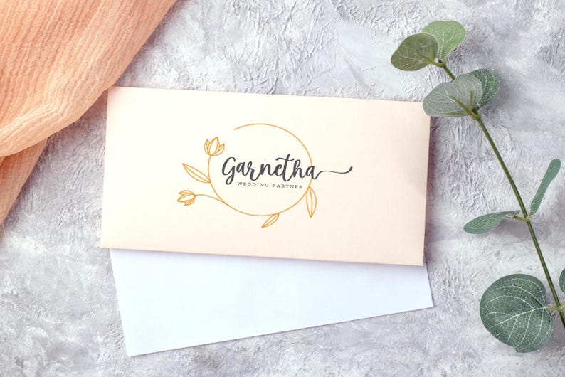 May include: A cream-colored card with a gold circle and floral design. The text "Garnetha Wedding Partner" is written in black cursive font.