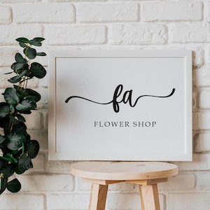 May include: White framed sign with black calligraphy that reads "fa FLOWER SHOP" against a white brick wall.