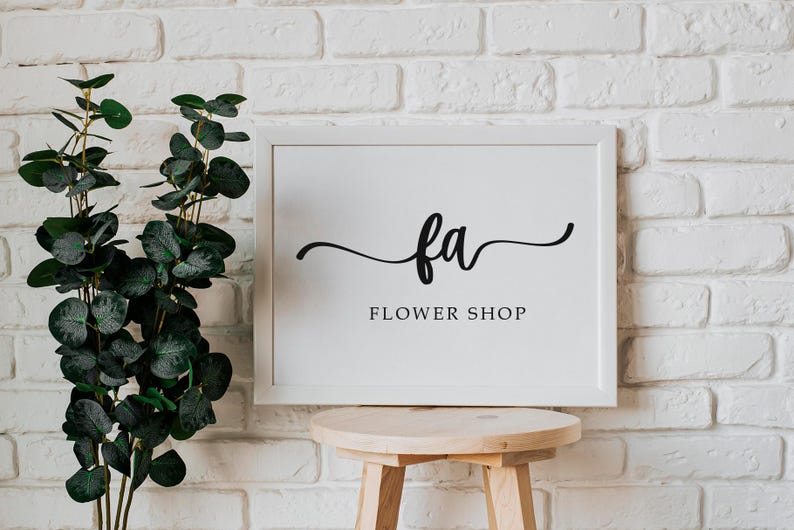 May include: White framed sign with black calligraphy that reads "fa FLOWER SHOP" against a white brick wall.