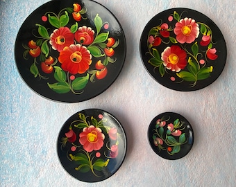 Puede incluir: Cuatro platos de madera pintados de negro con diseños florales. Los platos son de diferentes tamaños y presentan flores rojas, rosas, verdes y amarillas.