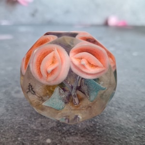 May include: A clear, faceted, geometric resin paperweight with pink and blue floral inclusions.