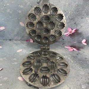Peut inclure: Un gaufrier en métal vintage de forme circulaire. Le gaufrier est composé de deux parties, l'une avec un motif de petits cercles et l'autre avec un motif de grands cercles. Le gaufrier est ouvert, révélant l'intérieur des moules à gaufres.