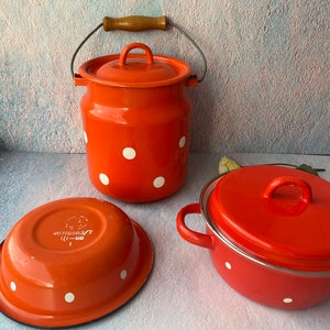 May include: A set of three orange enamelware kitchen items with white polka dots. The set includes a large pot with a lid and a handle, a smaller pot with a lid, and a bowl. The items are all made of enamelware and have a white polka dot pattern.