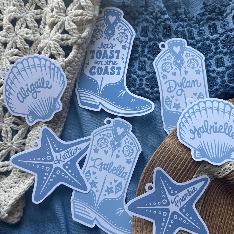 Puede incluir: Pegatinas troqueladas de color azul claro con tem&aacute;tica costera. Los dise&ntilde;os incluyen una concha con el nombre "Abigaile", una estrella de mar con "Kaitlin", una bota de vaquero con "Let's Toast on the Coast", otra bota con "Dylan", una concha con "Gabrielle", una bota con "Isabella" y una estrella de mar con "Frankie".