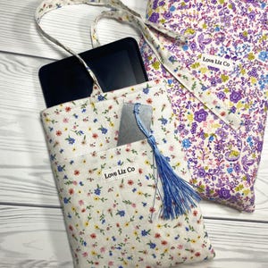 May include: Two floral fabric tote bags. One bag holds a black e-reader and a gray bookmark with a blue tassel. The other bag is visible in the background. Both bags have the text "Love Liz Co" on a white label.