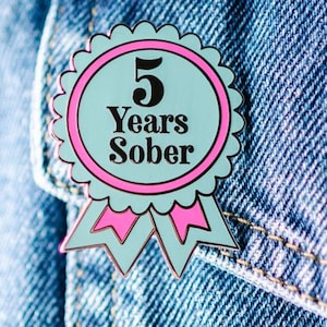 Könnte beinhalten: Eine blaue und rosafarbene Emaille-Anstecknadel mit einem weißen Band. Die Anstecknadel trägt die Aufschrift "5 Years Sober".