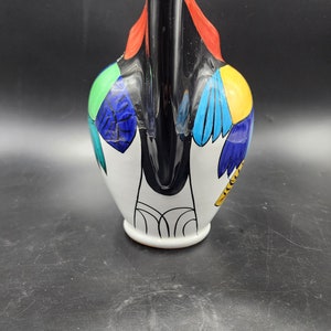 May include: A white ceramic pitcher with a black handle and colorful geometric designs. The pitcher features a red, yellow, blue, green, and black color scheme.