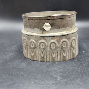 May include: A vintage metal cake tin with a fluted edge and a decorative design. The tin is made of two pieces, with a removable top.