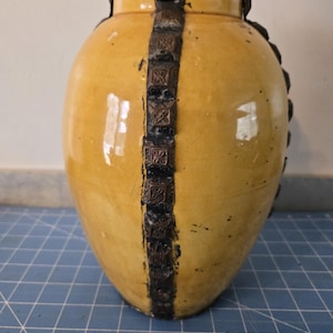 May include: A yellow ceramic vase with a decorative brown and black trim. The vase has a rounded shape and a glossy finish.