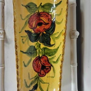 May include: A rectangular, hand-painted ceramic tray with a yellow background. The tray features two red roses with green leaves and stems. The edges are trimmed with a brown, scalloped border. The tray is a decorative piece.