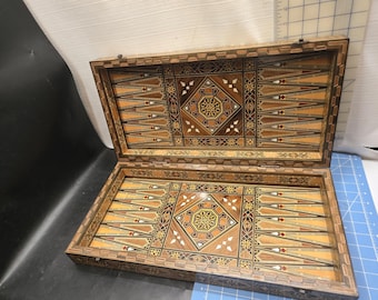 Op de afbeelding: Open houten backgammonbord met ingelegde geometrische patronen in bruin, beige en crème. Het rechthoekige bord heeft een scharnierend deksel, met gedetailleerd vakmanschap en een klassiek spelontwerp.