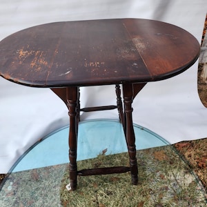 May include: A dark brown wooden oval drop leaf table with turned legs. The table is sitting on a blue and green patterned surface.