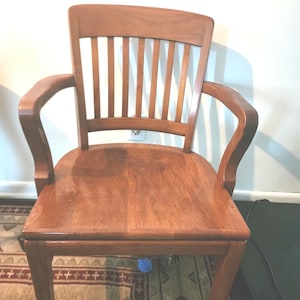 May include: A solid wood chair with a slatted back and curved arms. The chair is stained a rich brown color and has a simple, classic design.