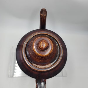 May include: A brown ceramic teapot with a lid and a handle. The teapot has a dark brown glaze and a slightly textured surface.