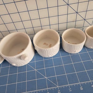 May include: Set of four white ceramic nesting bowls with a wood grain pattern. The bowls are different sizes and have a gold rim.