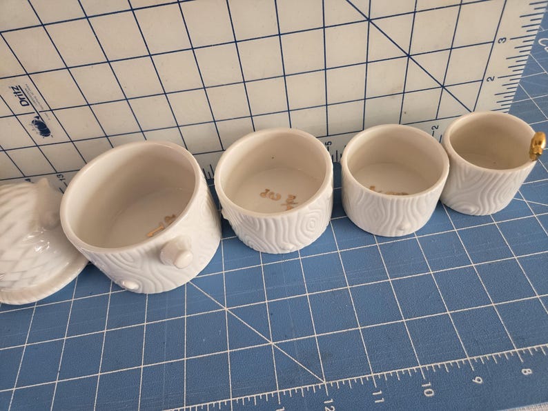 May include: Set of four white ceramic nesting bowls with a wood grain pattern. The bowls are different sizes and have a gold rim.