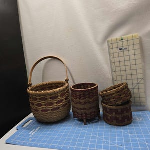 May include: A collection of woven baskets in various sizes. The baskets are made of natural and reddish-brown materials. One basket has a handle, and another has three small legs. A ruler is in the background.
