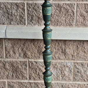 May include: A tall, green floor lamp with a decorative base and a chain hanging from the top. The lamp is made of metal and has a green and gold finish.