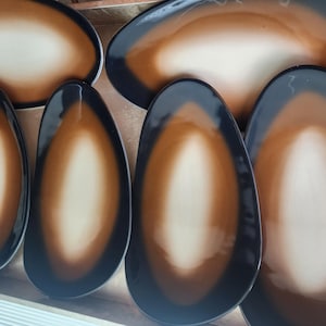 May include: Five oval-shaped ceramic plates with a brown and white ombre design. The plates are arranged in a row on a wooden surface.