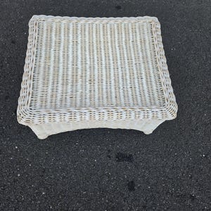 May include: A square, off-white wicker side table. The table has a woven top and a decorative border. The legs are curved and provide a sturdy base. This piece is suitable for indoor or outdoor use.