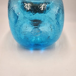 May include: A turquoise glass apple-shaped decorative object. The glass has a crackle finish, creating a textured surface. The apple has a stem and a rounded shape, with a glossy appearance.