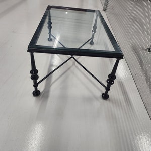 May include: A black metal coffee table with a glass top. The table has a simple, elegant design with four legs and a cross-shaped base.