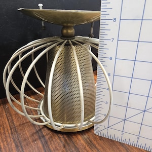 May include: A gold-toned metal lampshade with a white wire cage and a round, perforated metal base. The lampshade is about 7 inches tall.