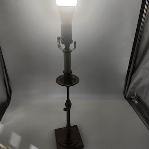 May include: A tall, antique-style table lamp with a bright white LED bulb. The lamp has a dark brown metal base and stem, with decorative brass accents. The lamp's base is square, and the stem has an adjustable height feature.