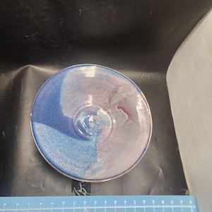 May include: A handmade ceramic bowl with a unique color scheme. The bowl features a gradient of blue and purple hues, with a glossy finish and a silver rim. The bowl's design is centered around a circular shape, perfect for serving or display.