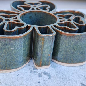 May include: A ceramic four-leaf clover shaped planter with a green and brown glaze. The planter has a raised rim and a cutout design in the center.