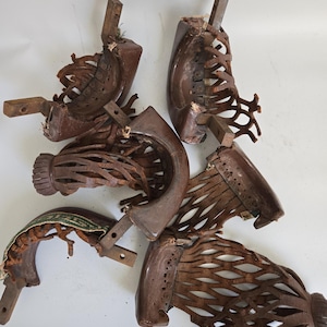 May include: A collection of antique, worn, and weathered brown pool table pocket liners. The liners are made of wood and leather, with intricate lattice-like designs. Some show signs of age and wear, with visible damage and fraying.