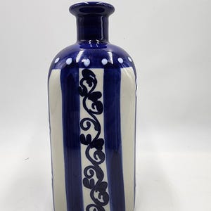 May include: A blue and white ceramic bottle with a decorative floral design. The bottle has a wide mouth and a narrow neck.
