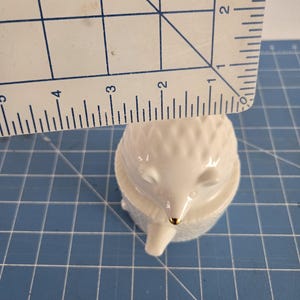 May include: White porcelain figurine of a hedgehog with a gold nose. The hedgehog is curled up in a ball with its eyes closed.