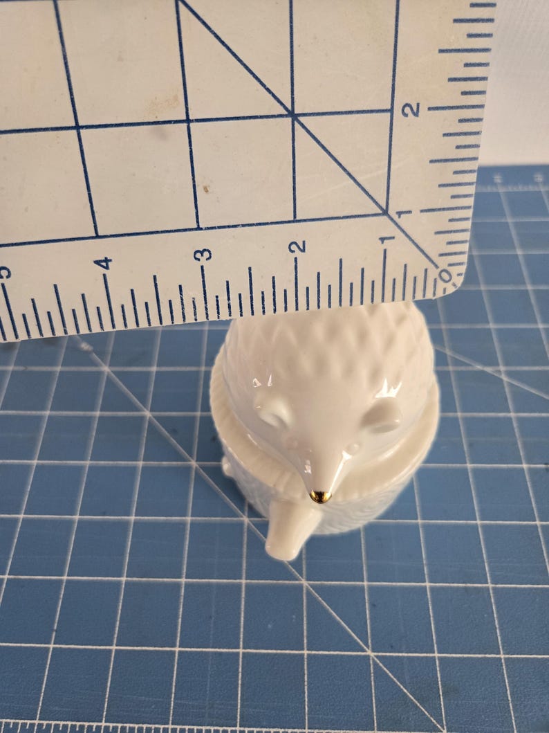 May include: White porcelain figurine of a hedgehog with a gold nose. The hedgehog is curled up in a ball with its eyes closed.