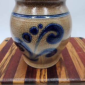 May include: A brown ceramic pot with a blue and white floral design. The pot has a textured surface and a rounded shape.