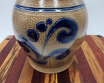 May include: A brown ceramic pot with a blue and white floral design. The pot has a textured surface and a rounded shape.