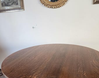 May include: A round wooden table with a dark brown finish. The table has a pedestal base with a carved design. The table is in a room with a gold mirror on the wall.