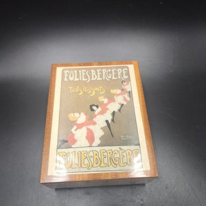 May include: A wooden box with a vintage poster of the Folies Bergere, a famous Parisian cabaret. The poster features a group of women in colorful costumes dancing. The text on the poster reads "Folies Bergere Tous les soirs".