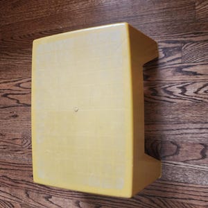 May include: A yellow plastic step stool with a textured surface.