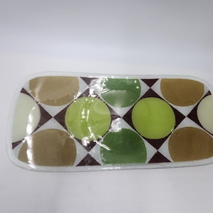 May include: A white rectangular glass serving tray with a geometric pattern of brown, green, and white circles on a brown and white checkered background.