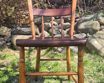 May include: A wooden chair with a dark brown finish, featuring a curved backrest with two horizontal slats, a contoured seat, and four turned legs connected by a central horizontal stretcher bar for structural support and stability.
