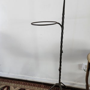 May include: A black wrought iron plant stand with a twisted stem and a circular top. The stand has a tripod base.