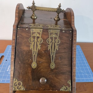 May include: Antique wooden boot or shoe storage box with brass hinges, handles, and accents. The box has a hinged lid and a small drawer.